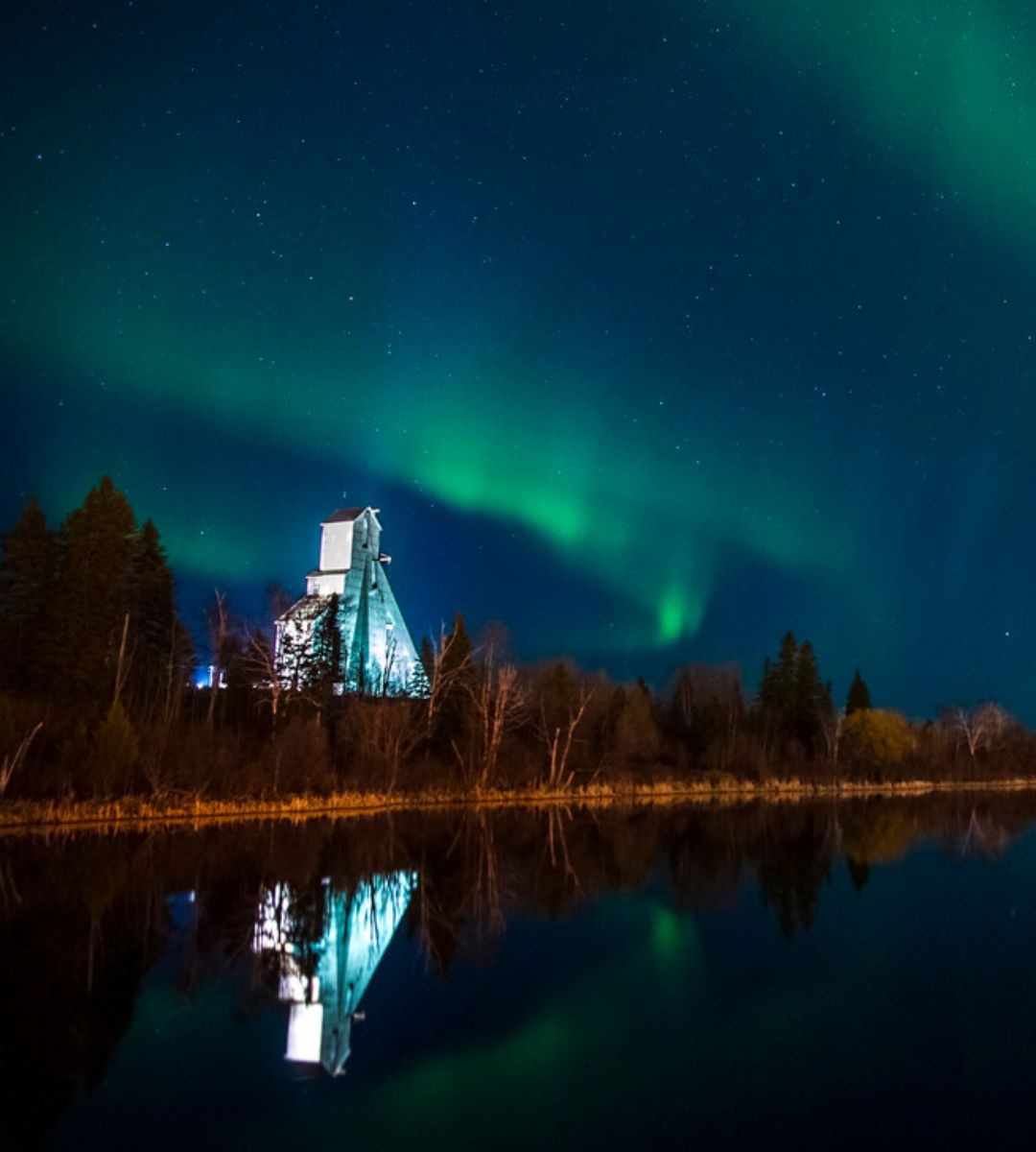 Timmins Care Aurora borealis over an industrial structure by a calm lake at night in Timmins. Cochrane District Social Services Administration Board